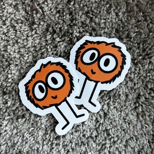 May include: Two orange fuzzy stickers with black eyes and a smiling mouth. Each sticker has two black legs.