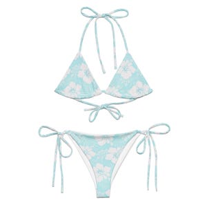 May include: A light blue bikini with a white floral print. The top is a triangle style with adjustable straps and ties at the back. The bottom is a cheeky style with ties on the sides.
