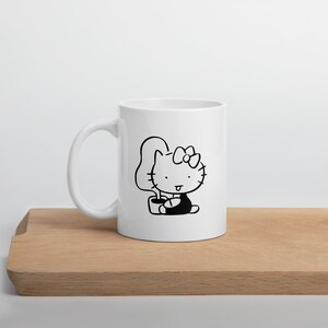 May include: White ceramic mug with a black line drawing of Hello Kitty sitting on a toilet.