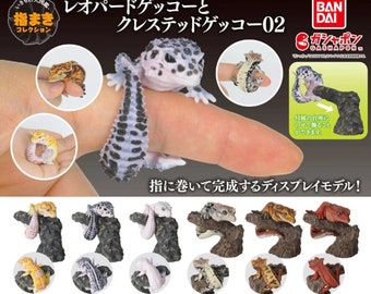 May include: A collection of miniature gecko figurines, including leopard and crested geckos, designed to wrap around a finger. The set features various color patterns and poses, with some geckos perched on miniature tree branches. The text on the image says "Leopard Gecko and Crested Gecko 02".