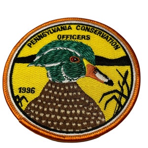 May include: A yellow and orange embroidered patch with a wood duck, the words "Pennsylvania Conservation Officers" and the year "1996".