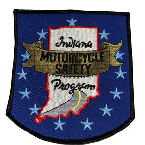 Puede incluir: Un parche azul con el texto "Indiana MOTORCYCLE SAFETY Program". El parche presenta el contorno del estado de Indiana en blanco, con un diseño de carretera amarilla. El parche está rodeado de estrellas azules.