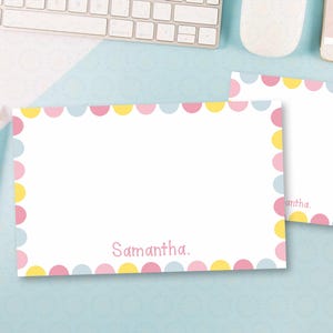 May include: White stationery set with a pastel scalloped border in pink, yellow, and blue. The stationery includes a notepad and a larger sheet, both with the name "Samantha" printed in pink. Pencils are visible on the left.