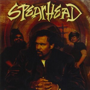 May include: Album cover featuring the band Spearhead. The band members are in the foreground, with the band's name in a stylized font at the top. The background has a reddish-brown hue.