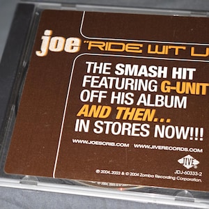 Könnte beinhalten: Eine CD-Hülle mit dem Albumcover von Joes "Ride Wit U". Das braune Etikett enthält den Text "The Smash Hit Featuring G-Unit" und "In Stores Now!!!" Die CD-Hülle ist transparent, und das Etikett hat weißen und orangefarbenen Text.