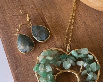 Puede incluir: Un collar de oro con un colgante en forma de corazón que representa el árbol de la vida, hecho con piedras verdes. El collar viene con un par de pendientes a juego con piedras en forma de lágrima.