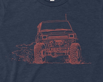 Op de afbeelding: Een marineblauw t-shirt met een rode lijntekening van een jeep op de voorkant. De jeep is naar voren gericht en heeft grote banden.