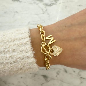 May include: Gold chain bracelet with a heart charm and a letter 'W' charm. The heart charm is encrusted with clear rhinestones.