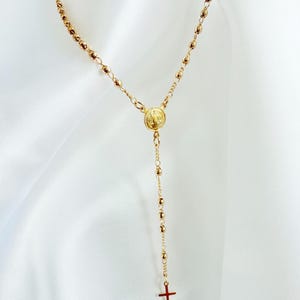 Peut inclure: Collier de chapelet dor&eacute; avec un pendentif en forme de croix. Le collier est compos&eacute; de petites perles rondes et d'un m&eacute;daillon circulaire. La croix et le m&eacute;daillon sont &eacute;galement dor&eacute;s. Le collier est pr&eacute;sent&eacute; sur un fond blanc.