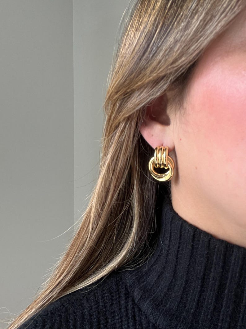 Op de afbeelding: Gouden creolen met een gedraaid ontwerp. De oorbellen worden gedragen door een persoon met lang bruin haar.
