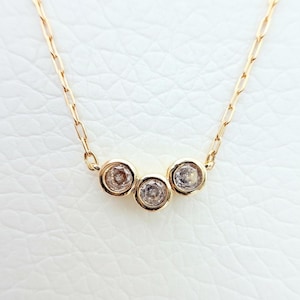 May include: A delicate gold necklace featuring three small, round, clear gemstones set in individual bezels. The chain is a fine, linked design. The necklace is displayed against a white background, highlighting the jewelry's sparkle and design.
