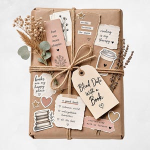 May include: A wrapped gift with a tag that says "Blind Date With a Book." The gift is decorated with paper cutouts, twine, and dried flowers. Text on the cutouts includes "books are my happy place" and "reading is my therapy."