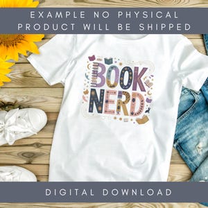 May include: White t-shirt with the words "BOOK NERD" in colorful, whimsical lettering. The design includes illustrations of books, stars, and other decorative elements. The shirt is displayed on a wooden surface.