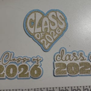 three glittery heart-shaped cutouts with the text "CLASS OF 2026" written on them, likely representing a graduation or class of 2026 event.
