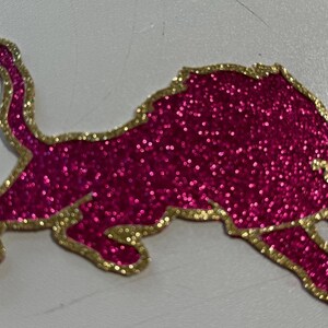 A pink glittery lion sticker or decal with a gold border.