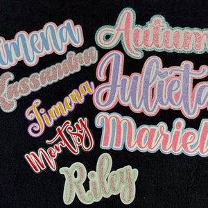 May include: A collection of custom name cutouts featuring glittery and solid cardstock lettering. The names Jimena, Kassandra, Autumn, Julieta, Mariel, Montsy, and Riley are displayed in various cursive fonts, vibrant colors, and layered outlines.