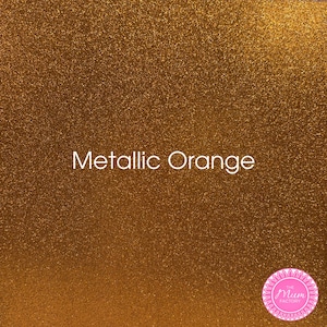 May include: A sheet of metallic orange glitter material with a dense, sparkling texture. The text Metallic Orange is printed in white in the center. A circular pink logo with the text The Mum Factory is located in the bottom right corner.