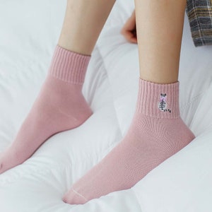 May include: A pair of pink ankle socks with a small embroidered cat design on one sock.