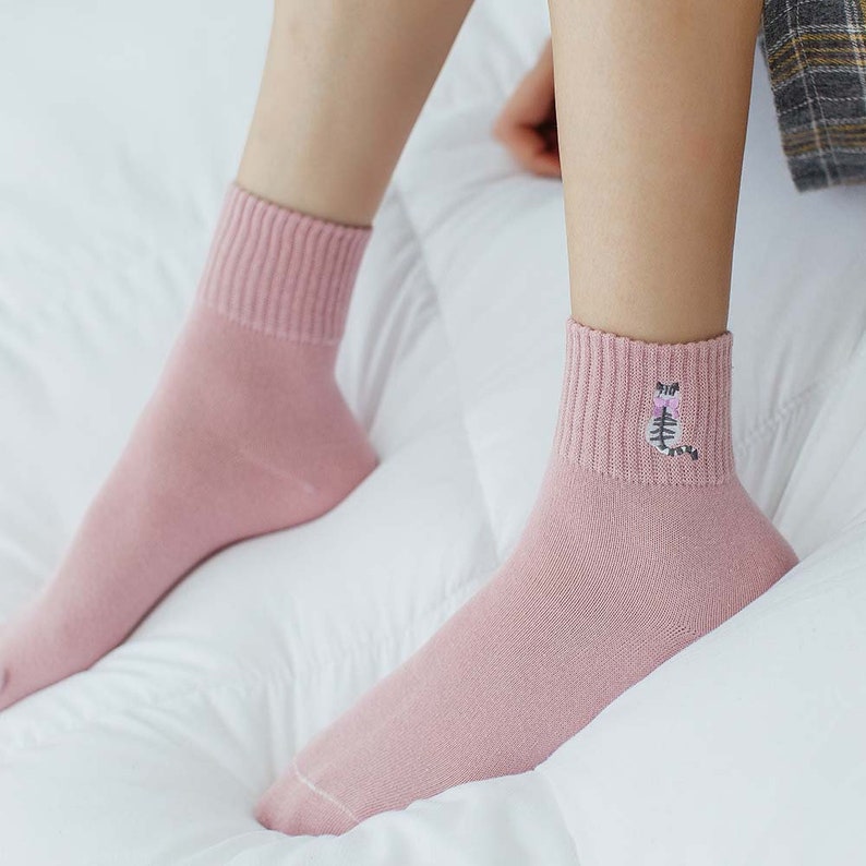 May include: A pair of pink ankle socks with a small embroidered cat design on one sock.