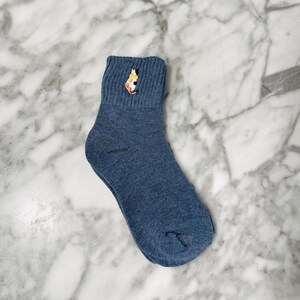 May include: A pair of blue ankle socks with a colorful cat embroidered on the top of the sock.