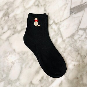May include: Black ankle socks with a small embroidered cat wearing a red bow tie.