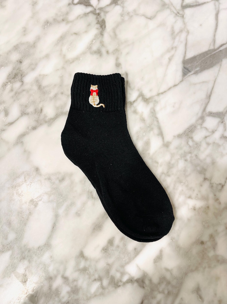 May include: Black ankle socks with a small embroidered cat wearing a red bow tie.