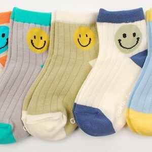 May include: Five pairs of colorful socks with a smiley face design. The socks are made of a soft, comfortable material and have a ribbed texture. The socks are available in a variety of colors, including orange, gray, green, white, and blue.