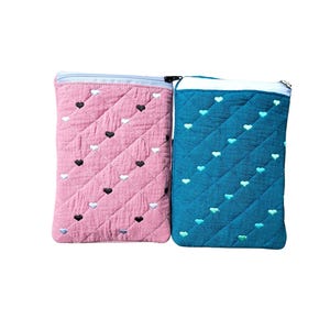 May include: Two quilted fabric pouches. One is pink with black and white heart embroidery, the other is teal with teal heart embroidery. Both have a diagonal quilted pattern and a zip closure at the top.