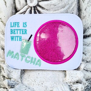 May include: White rectangular patch with the text "LIFE IS BETTER WITH MATCHA" in teal. A pink glittery circle and a green matcha drink with a straw are also featured on the patch.