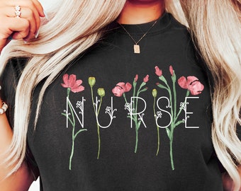 May include: Black t-shirt with the word "NURSE" written in white with floral accents. The flowers are pink and green.