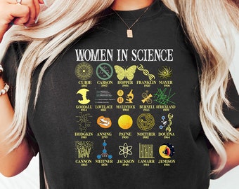 May include: A black t-shirt featuring a graphic of a circle containing the names of women in science and their respective fields. The text "Women in Science" is at the top of the graphic.