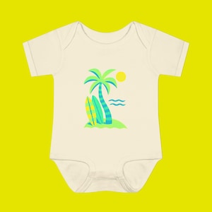 Peut inclure: Body bébé crème avec une scène de plage tropicale. Le motif comprend un palmier, deux planches de surf, un soleil jaune et des vagues océaniques vertes et bleues. Le body est à manches courtes.