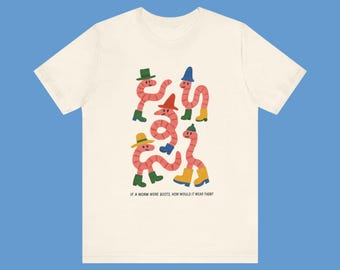 Op de afbeelding: Crèmekleurig T-shirt met een grillige illustratie van roze wormen met hoeden en laarzen in verschillende kleuren. De tekst onderaan luidt: "IF A WORM WORE BOOTS, HOW WOULD IT WEAR THEM?"