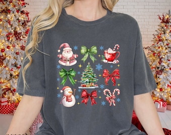 May include: Dark grey t-shirt with a Christmas-themed design. The design includes Santa Claus, green bows, a Christmas tree, a snowman, red bows, a cup of hot cocoa, candy canes, and snowflakes. The word "pepper" is printed on the bottom left.