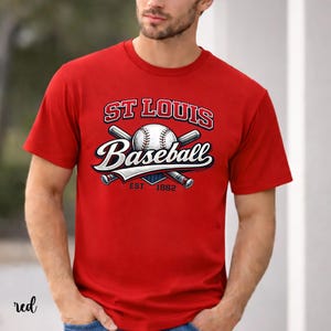 Puede incluir: Camiseta roja con un gráfico de béisbol. El gráfico incluye el texto "ST LOUIS Baseball" encima de una pelota de béisbol y bates cruzados, con "EST 1882" debajo. La palabra "red" está escrita en la esquina inferior izquierda.