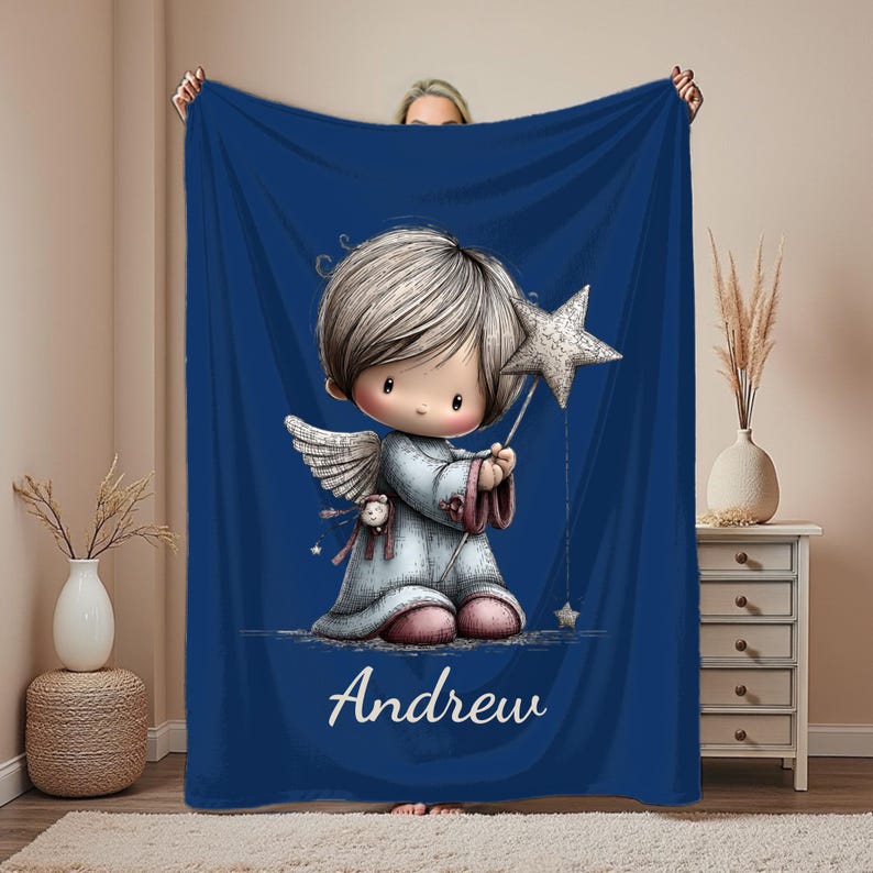 May include: A navy blue blanket featuring a cartoon angel holding a star wand. The angel has light brown hair, wings, and is wearing a light blue robe. The name "Andrew" is written in white script at the bottom.