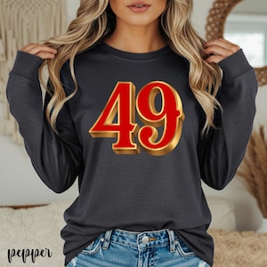 May include: Dark gray long-sleeve shirt with a large, red and gold number 49 graphic on the front. The number has a 3D effect. The shirt is made of a soft material.