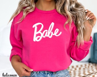 May include: A pink sweatshirt with the word "Babe" in white script on the front.