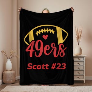 May include: Black blanket featuring a yellow and red American football design. The blanket has the text "49ers" in red script, with a heart above it. The text "Scott #23" is also in red.