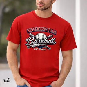 Puede incluir: Camiseta roja con un gráfico de béisbol. El gráfico presenta las palabras "WASHINGTON Baseball" en un diseño estilizado, con una pelota de béisbol y bates cruzados. También se incluye el texto "EST - 1969".