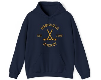 May include: Navy blue hoodie with a front pocket and drawstring hood. The front features a gold design with the words "NASHVILLE HOCKEY" and crossed hockey sticks. The text "EST. 1998" is also included in the design.