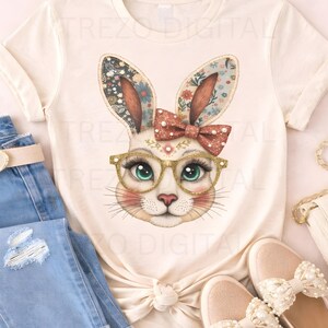 May include: A cream-coloured t-shirt with a bunny face design. The bunny has floral ears, a red bow, and gold-rimmed glasses. The shirt is styled with blue jeans, a belt, and pink shoes. The bunny has green eyes and rosy cheeks.