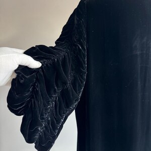 K&ouml;nnte beinhalten: Ein schwarzes Samtkleid mit langen &Auml;rmeln. Die &Auml;rmel sind gerafft und haben einen ger&uuml;schten Look.