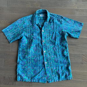 Könnte beinhalten: Ein blaues, kurzärmeliges Hemd mit Knöpfen und einem floralen und gestreiften Muster.