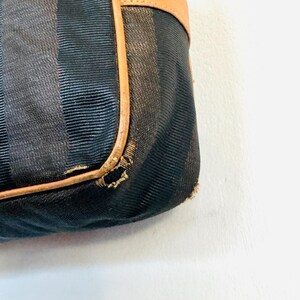 May include: Close-up of a black and brown striped fabric handbag with a brown leather trim. The fabric has a subtle texture and the leather trim is slightly worn.