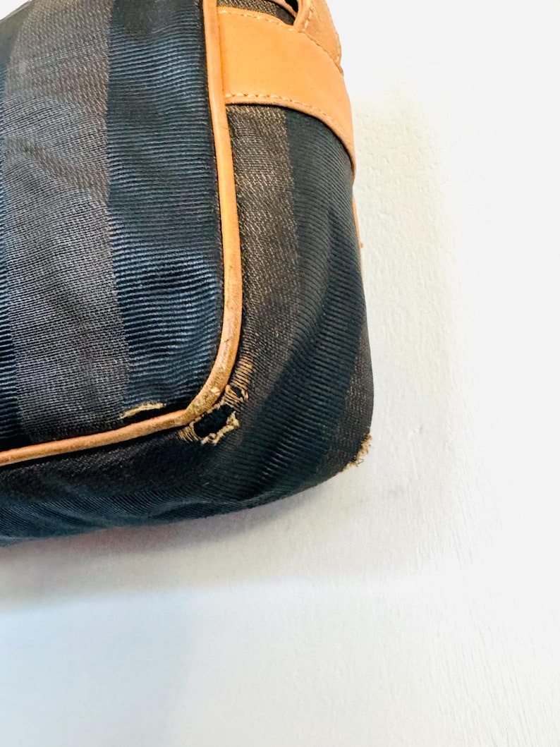 May include: Close-up of a black and brown striped fabric handbag with a brown leather trim. The fabric has a subtle texture and the leather trim is slightly worn.