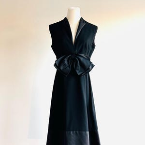 May include: A black sleeveless dress with a large satin bow at the waist. The dress has a V-neckline and a flared skirt.
