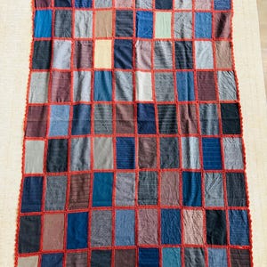 May include: A patchwork quilt made from squares of different colored fabrics, sewn together with red thread. The quilt has a crocheted border.