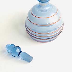 Pu&ograve; includere: Una bottiglia di vetro blu con un design a strisce e un tappo di vetro blu abbinato. La bottiglia ha un corpo rotondo e un collo stretto.