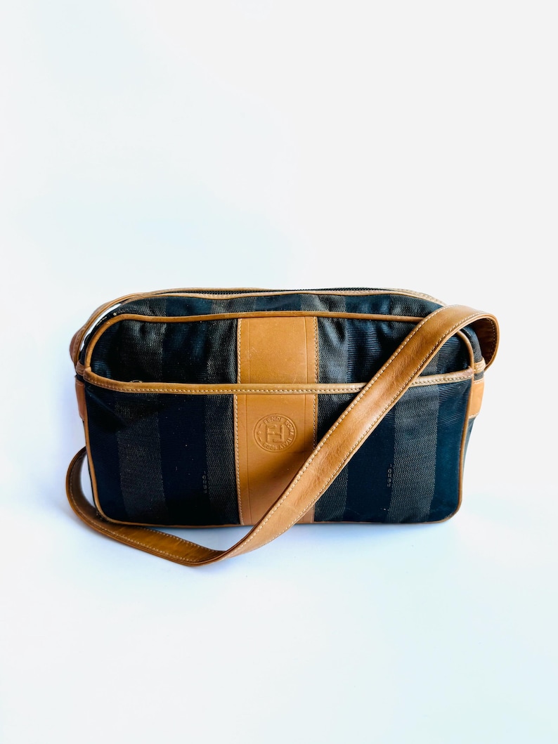 May include: A brown and black striped shoulder bag with a brown leather strap and a brown leather patch with the letter "F" in the center.